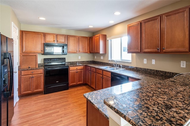 kitchen with dark stone countertops, sink, kitchen peninsula, and black appliances