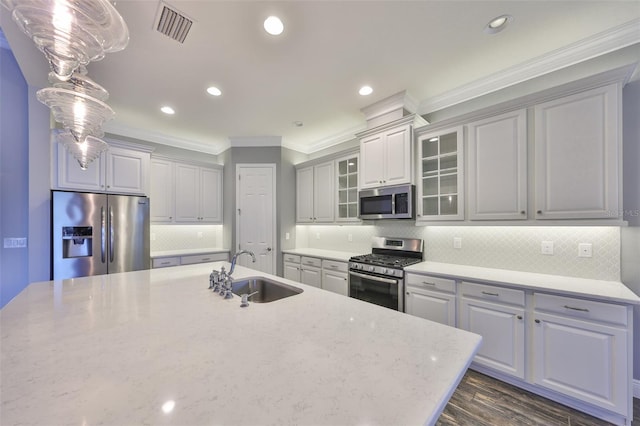 kitchen with sink, light stone counters, ornamental molding, pendant lighting, and stainless steel appliances