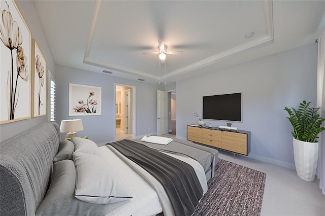 carpeted bedroom with a raised ceiling, ceiling fan, and ensuite bath