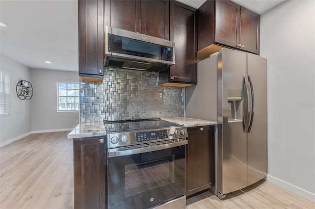 kitchen with appliances with stainless steel finishes, light wood-type flooring, light stone counters, and decorative backsplash