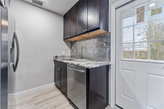 kitchen with dark brown cabinetry, sink, appliances with stainless steel finishes, light stone countertops, and decorative backsplash