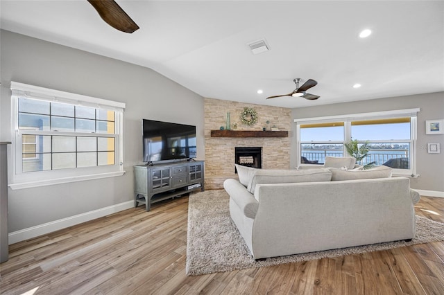 living room with vaulted ceiling, a stone fireplace, ceiling fan, and light hardwood / wood-style floors