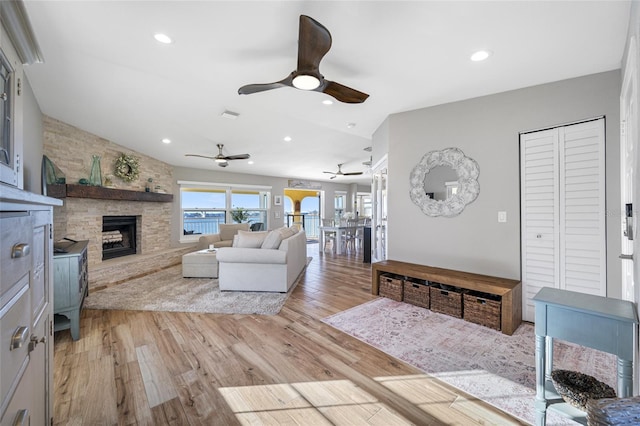 living room with ceiling fan, a stone fireplace, and light hardwood / wood-style floors