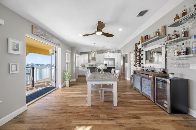 kitchen with wall chimney range hood, hardwood / wood-style flooring, stainless steel fridge, white cabinetry, and beverage cooler