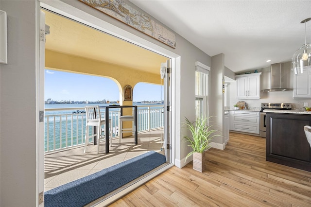 interior space with light hardwood / wood-style flooring, white cabinetry, a water view, stainless steel range with electric cooktop, and wall chimney exhaust hood