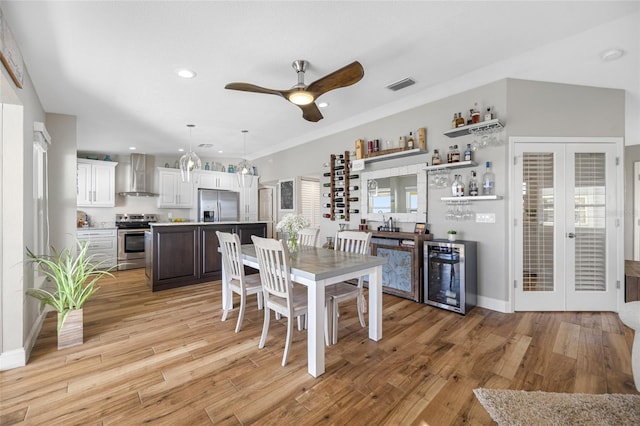 kitchen with light hardwood / wood-style flooring, appliances with stainless steel finishes, white cabinetry, beverage cooler, and wall chimney exhaust hood