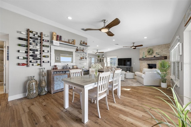 dining room featuring light hardwood / wood-style flooring, a large fireplace, ceiling fan, and vaulted ceiling