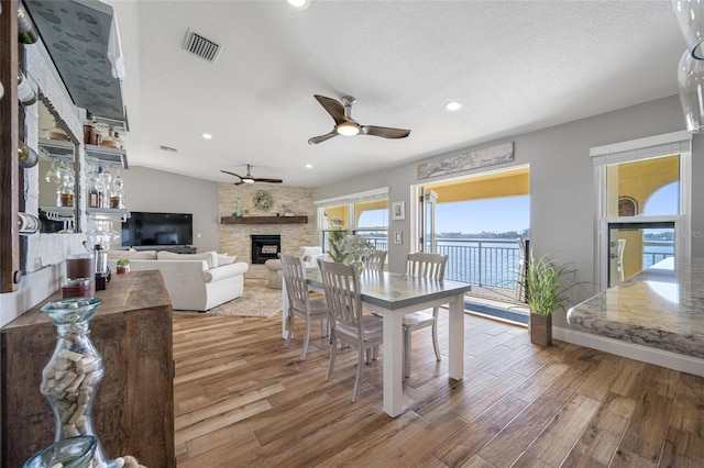 dining area with vaulted ceiling, a textured ceiling, ceiling fan, a fireplace, and hardwood / wood-style floors