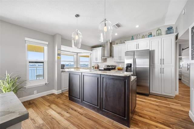 kitchen with wall chimney exhaust hood, white cabinetry, a center island, pendant lighting, and stainless steel appliances