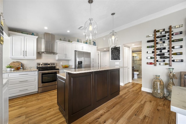 kitchen featuring appliances with stainless steel finishes, decorative light fixtures, white cabinetry, a center island, and wall chimney range hood