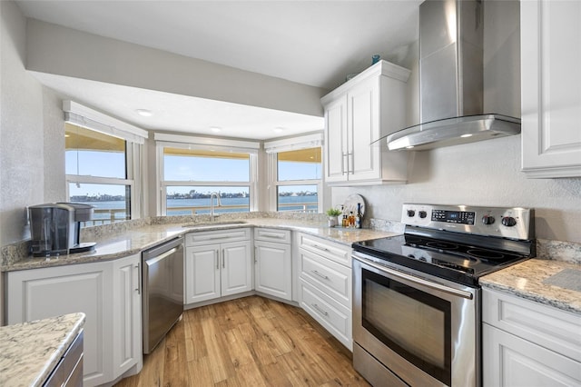 kitchen with appliances with stainless steel finishes, sink, white cabinets, a water view, and wall chimney exhaust hood