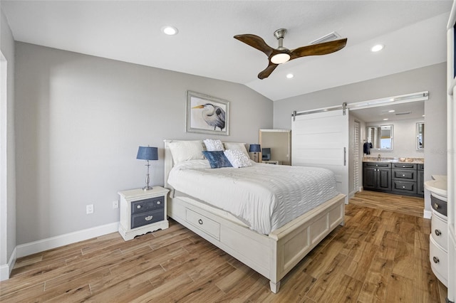 bedroom featuring vaulted ceiling, a barn door, ensuite bathroom, and light hardwood / wood-style floors