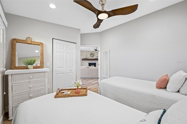 bedroom with lofted ceiling, light hardwood / wood-style flooring, a closet, ceiling fan, and a fireplace