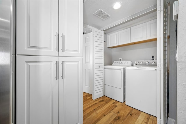 clothes washing area with washing machine and dryer, cabinets, and light wood-type flooring