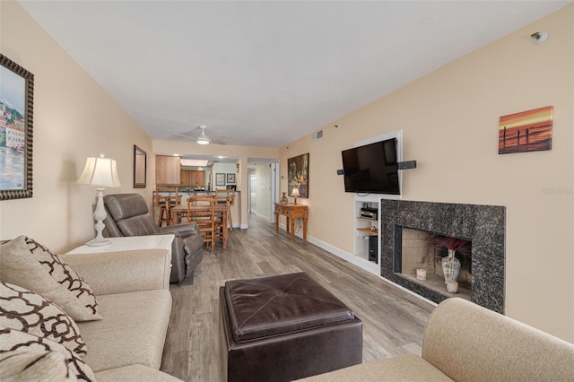 living room featuring ceiling fan, a fireplace, and light wood-type flooring