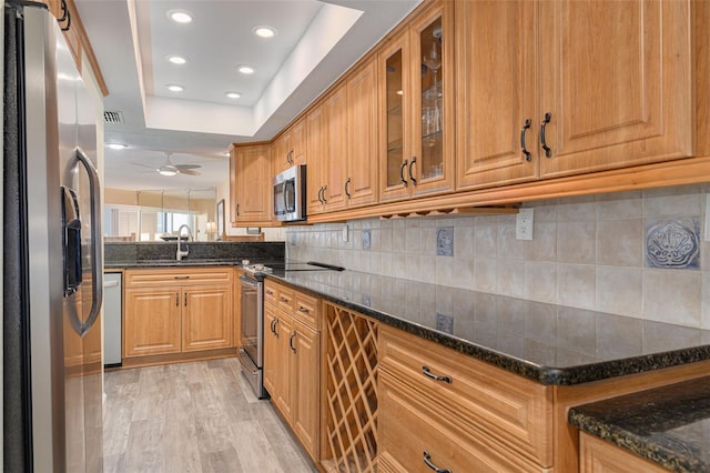 kitchen with sink, tasteful backsplash, light wood-type flooring, dark stone countertops, and appliances with stainless steel finishes