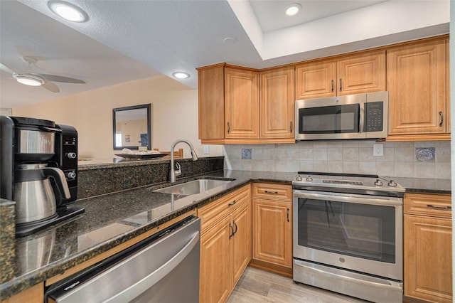 kitchen featuring sink, light hardwood / wood-style flooring, dark stone countertops, stainless steel appliances, and tasteful backsplash