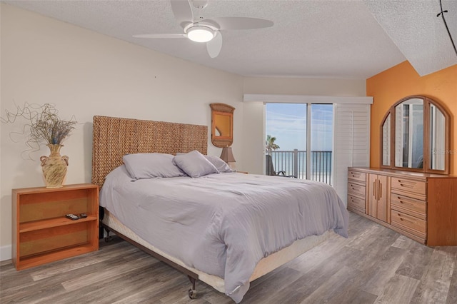 bedroom with ceiling fan, hardwood / wood-style floors, a textured ceiling, and access to outside