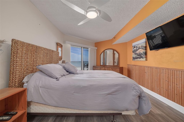 bedroom featuring a textured ceiling, access to outside, wooden walls, dark hardwood / wood-style floors, and ceiling fan