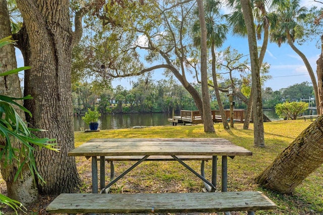 surrounding community with a deck with water view and a yard