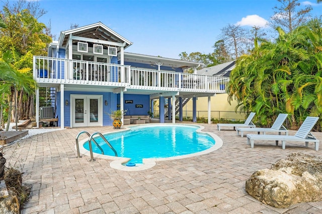 rear view of property with stairs, french doors, a wooden deck, an outdoor pool, and a patio area