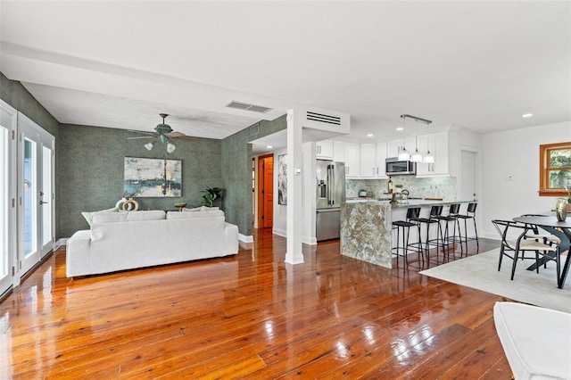 living area with a ceiling fan, wood-type flooring, visible vents, and baseboards