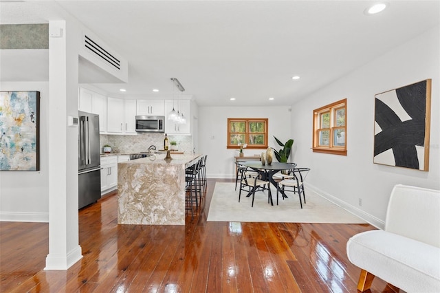 kitchen featuring dark wood-style floors, a center island with sink, stainless steel appliances, decorative backsplash, and white cabinetry