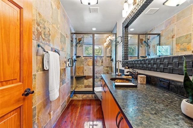 bathroom featuring toilet, wood finished floors, vanity, tile walls, and a stall shower