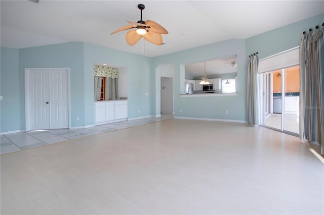 unfurnished living room with ceiling fan, arched walkways, lofted ceiling, and baseboards