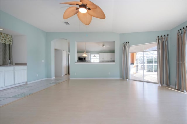 unfurnished living room featuring a ceiling fan, visible vents, vaulted ceiling, and baseboards