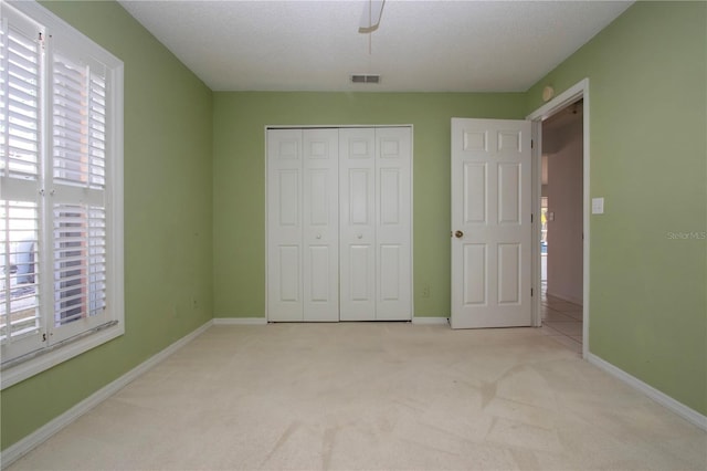 unfurnished bedroom featuring light carpet, a closet, visible vents, and baseboards