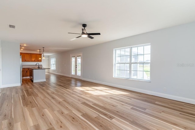 unfurnished living room with sink, french doors, ceiling fan, and light wood-type flooring