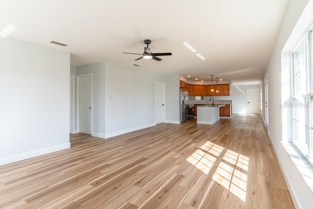 unfurnished living room featuring ceiling fan, light hardwood / wood-style floors, and sink