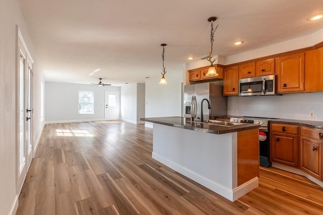 kitchen featuring decorative light fixtures, a kitchen island with sink, ceiling fan, light hardwood / wood-style floors, and stainless steel appliances