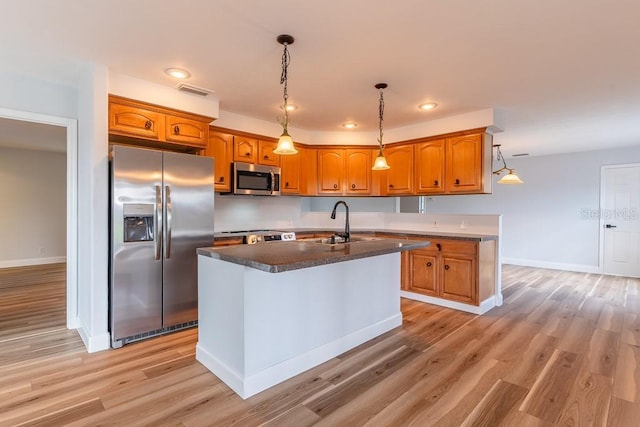 kitchen featuring sink, a kitchen island with sink, stainless steel appliances, light hardwood / wood-style floors, and decorative light fixtures