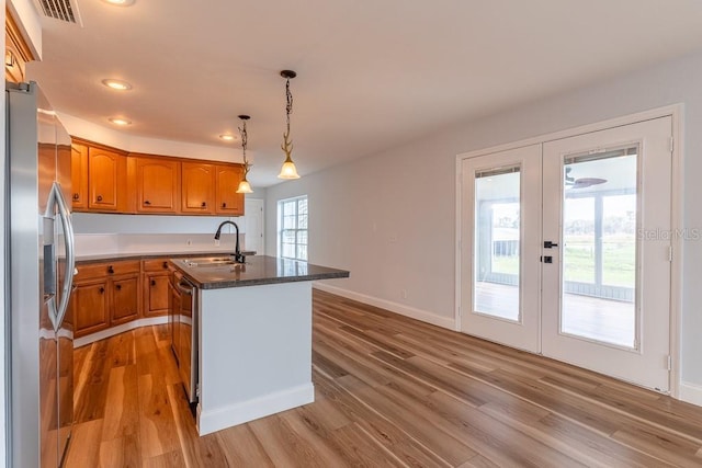 kitchen featuring an island with sink, sink, hanging light fixtures, stainless steel appliances, and french doors