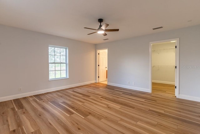 empty room with ceiling fan, a walk in closet, light hardwood / wood-style floors, and a closet