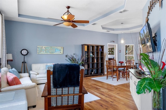 living room featuring ceiling fan, a raised ceiling, and light wood-type flooring