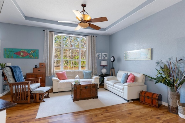 living room with light hardwood / wood-style flooring, a raised ceiling, and ceiling fan