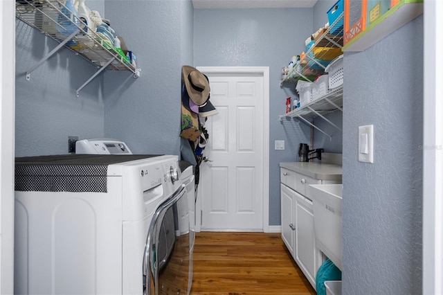 clothes washing area featuring cabinets, wood-type flooring, and washer and dryer