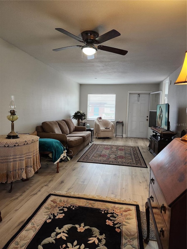 living room with ceiling fan, a textured ceiling, and light wood-type flooring