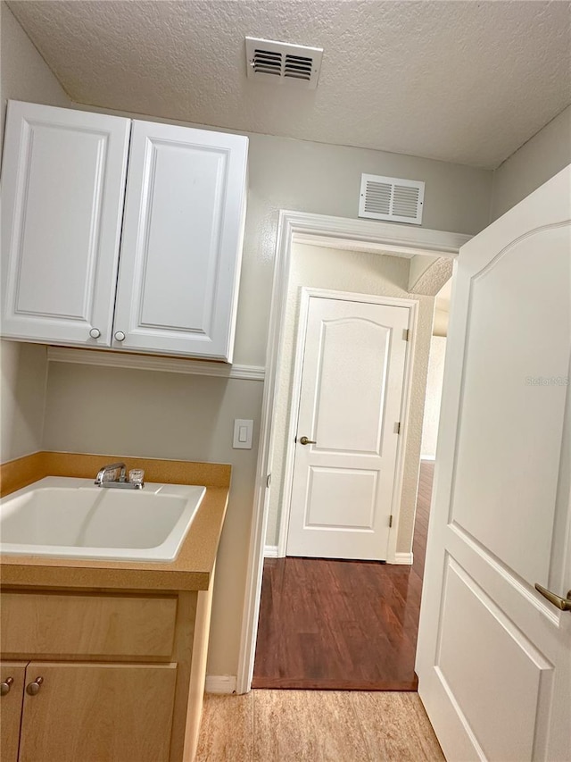 laundry room featuring sink, light hardwood / wood-style flooring, and a textured ceiling