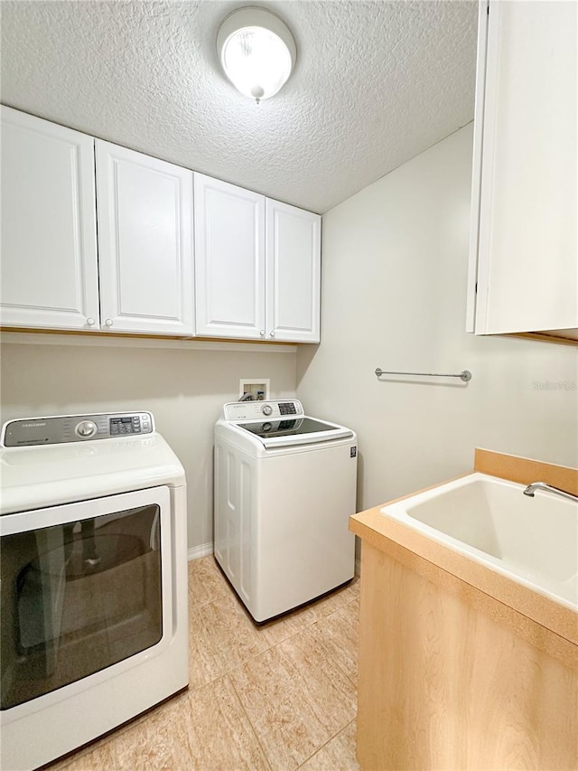 clothes washing area featuring sink, a textured ceiling, cabinets, and washing machine and clothes dryer