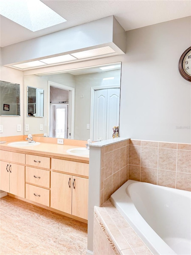 bathroom featuring vanity, a skylight, and tiled tub