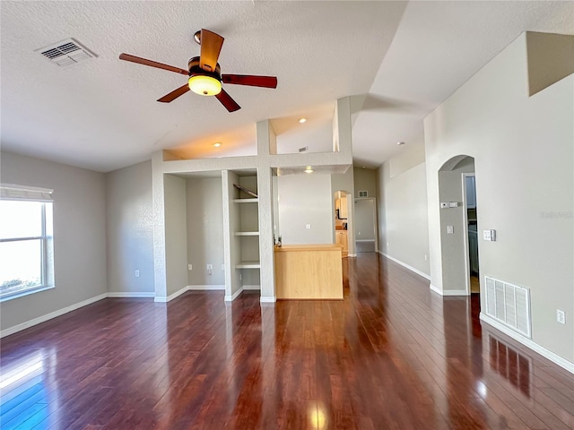 unfurnished living room featuring dark wood-type flooring, built in features, vaulted ceiling, and a textured ceiling