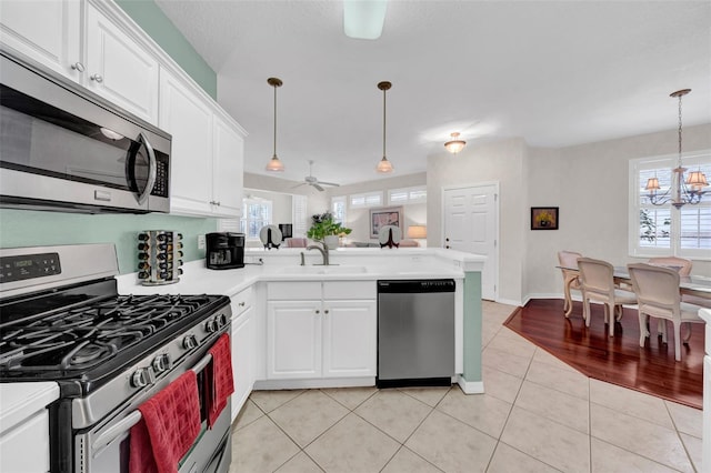 kitchen featuring pendant lighting, sink, stainless steel appliances, white cabinets, and kitchen peninsula