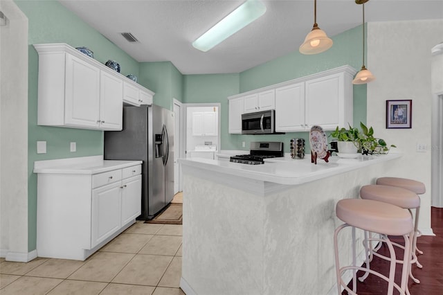 kitchen with stainless steel appliances, hanging light fixtures, white cabinets, and kitchen peninsula