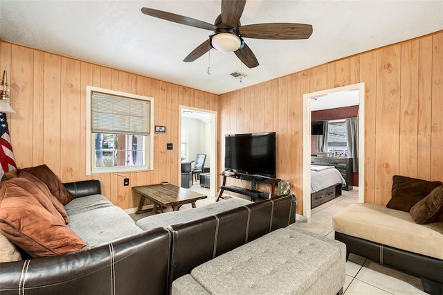 living room featuring ceiling fan, wood walls, and light tile patterned floors