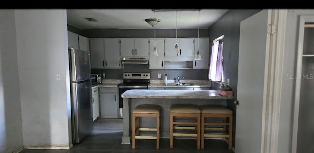 kitchen with stainless steel appliances, kitchen peninsula, a breakfast bar area, and white cabinets