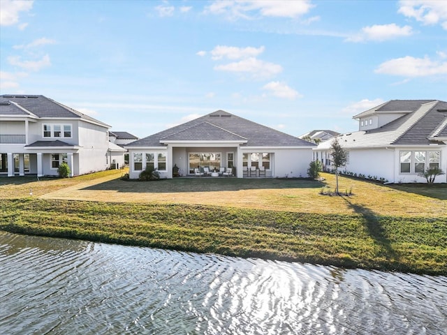 back of property with a water view and a lawn